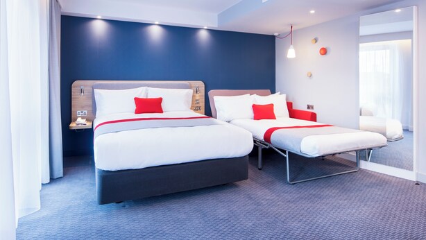 A hotel room with two beds, a nightstand, a lamp, and a window with curtains. - Holiday Inn Express Wigan by IHG (Wigan)