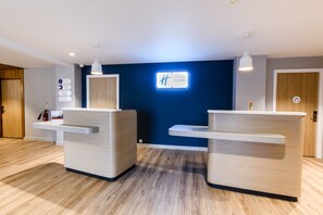 Un espace d’accueil avec deux comptoirs de réception, un mur bleu orné d’une enseigne « Holiday Inn Express » et une porte en bois.