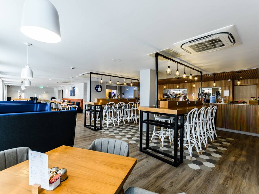 A modern restaurant with high tables, booths, and a bar area.