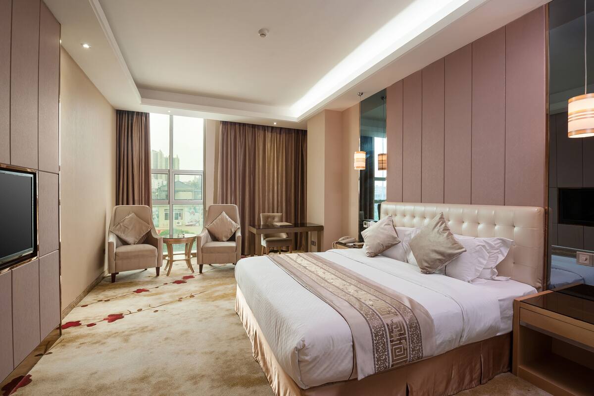 A hotel room with a large bed, a TV, a desk, and a chair.