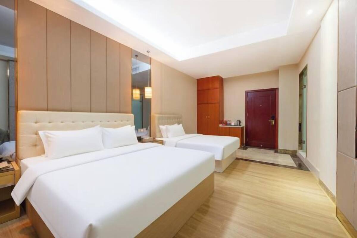 A hotel room with two beds, a wooden headboard, a small kitchenette, and a red door.