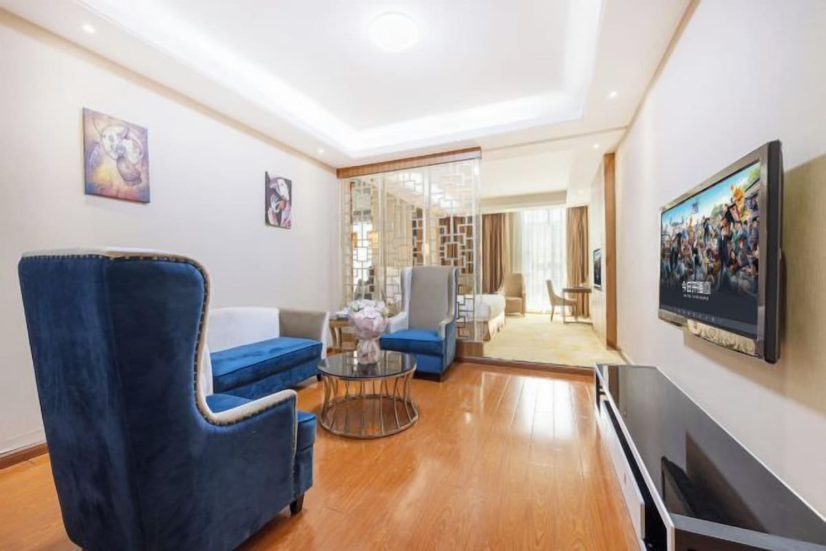 Una sala de estar moderna con un sillón azul, una mesa de centro de vidrio y un televisor de pantalla plana montado en la pared.