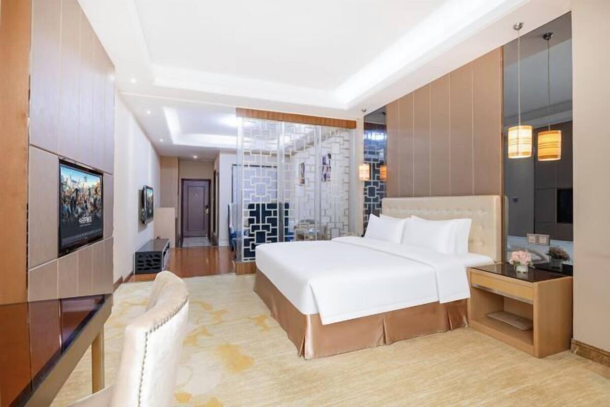 A hotel room with a large bed, a TV, a desk, and a mirror.