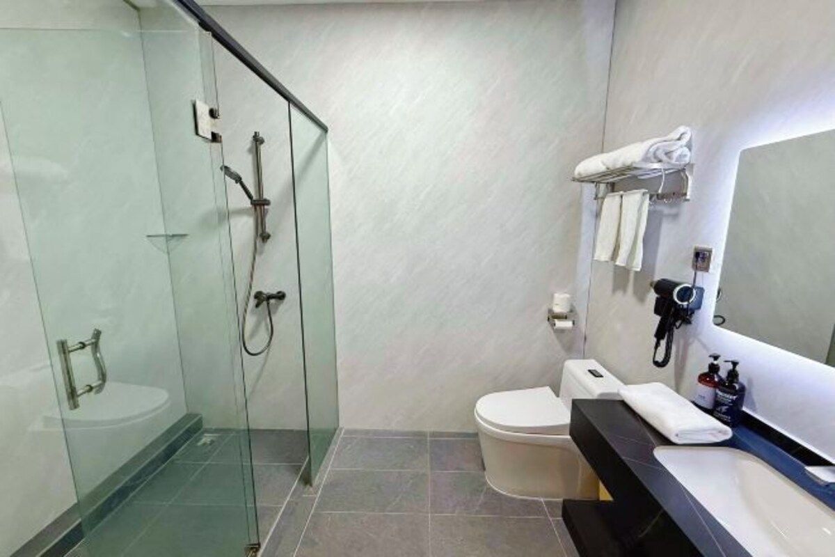 A modern bathroom with a glass-enclosed shower, a toilet, and a sink with a towel rack.