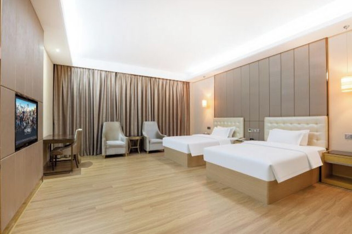 A hotel room with two beds, a desk, a chair, and a TV.