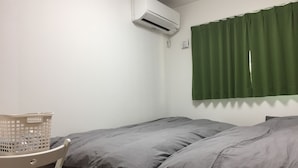 A small, simple room with a bed, a chair, and a laundry basket. - Shonan Enoshima Seaside Guest House ANNEX (Kamakura)