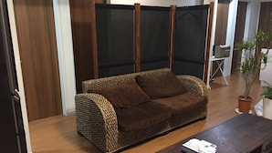 A living room with a brown sofa, a coffee table with books, a potted plant, and a sliding door. - Shonan Enoshima Seaside Guest House ANNEX (Kamakura)