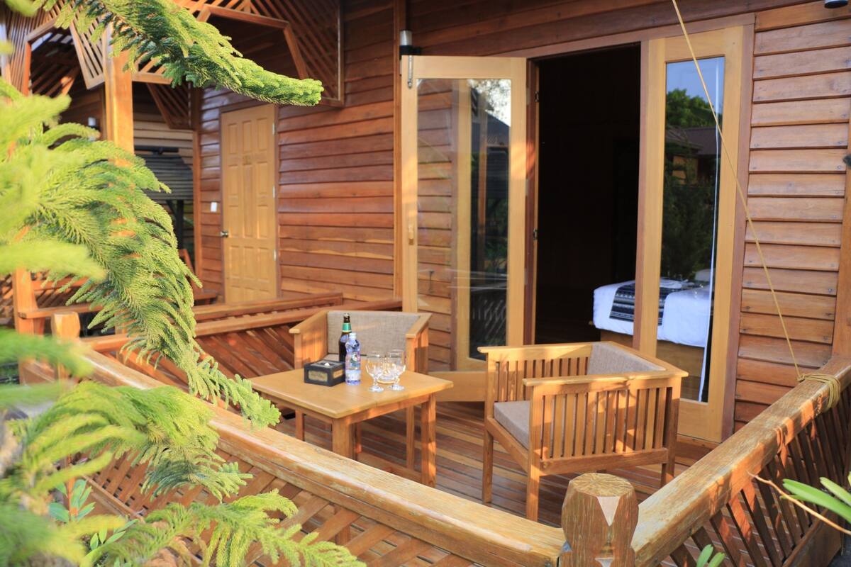 A wooden deck with a table and chairs, a door leading to a room, and a window with a view.