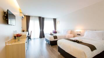 A hotel room with two beds, a desk, a chair, a TV, and a window with curtains.
