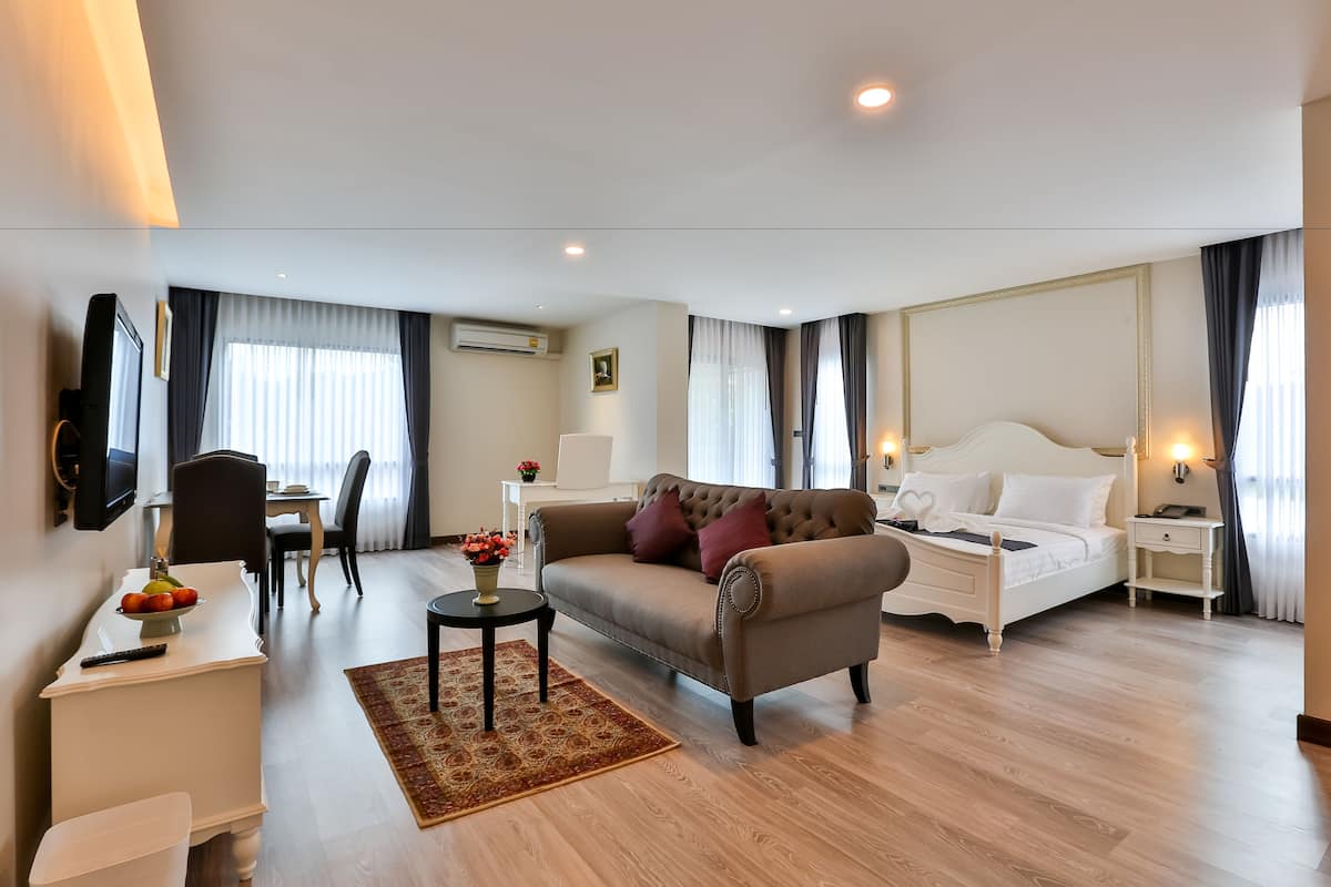 A hotel room with a sofa, a bed, a desk with a chair, a TV, and a dining area.