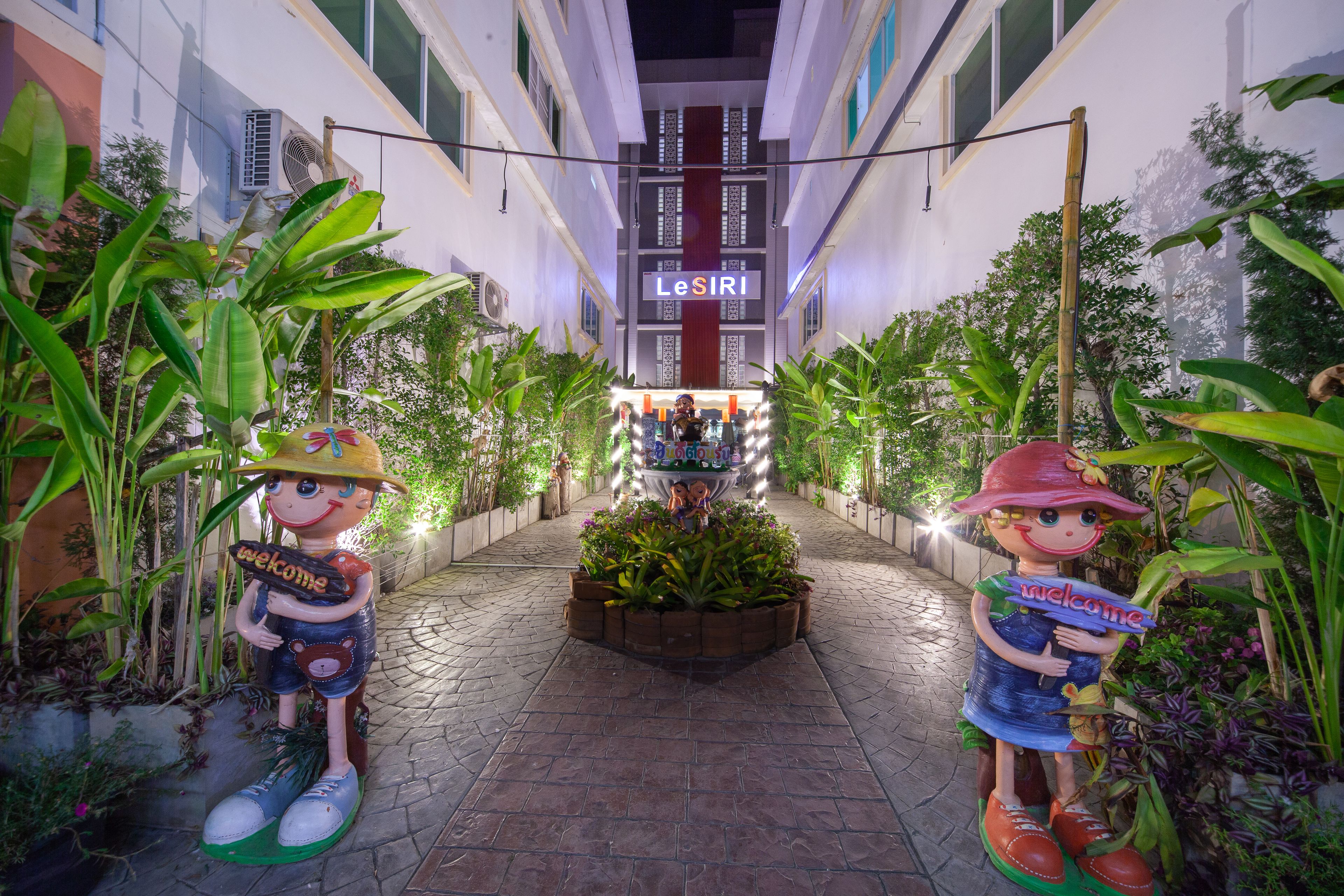 A pathway leading to a building with a 'LeSIRI' sign, flanked by decorative statues and lush greenery.