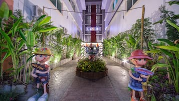 Un sendero lleva a un edificio con el letrero 'LeSIRI', flanqueado por estatuas decorativas y exuberante vegetación.