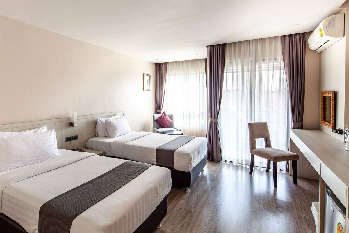 A hotel room with two beds, a desk, a chair, a mirror, and a window with curtains.