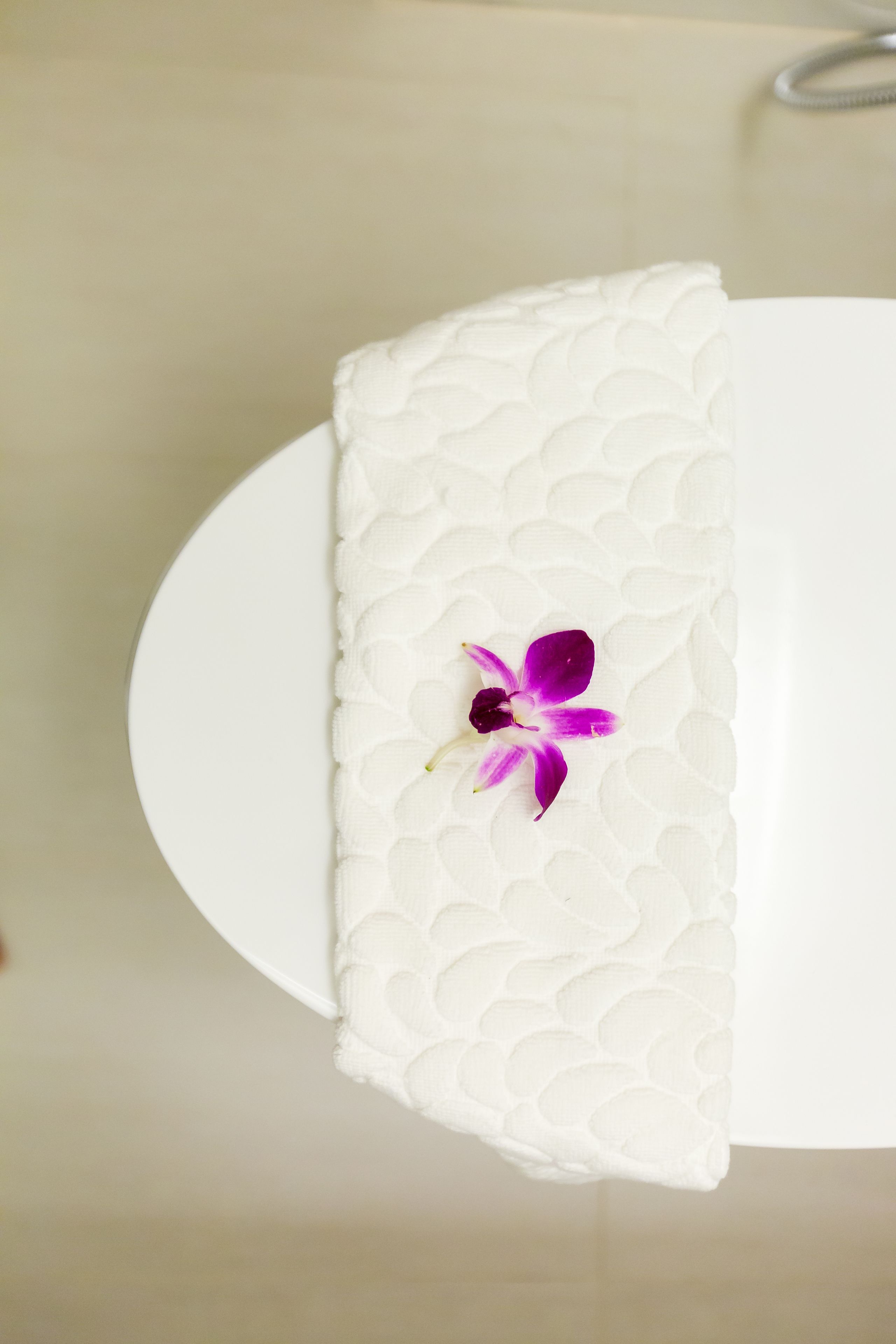 Ein weißer Tisch mit einer strukturierten weißen Serviette und einer violetten Orchidee.