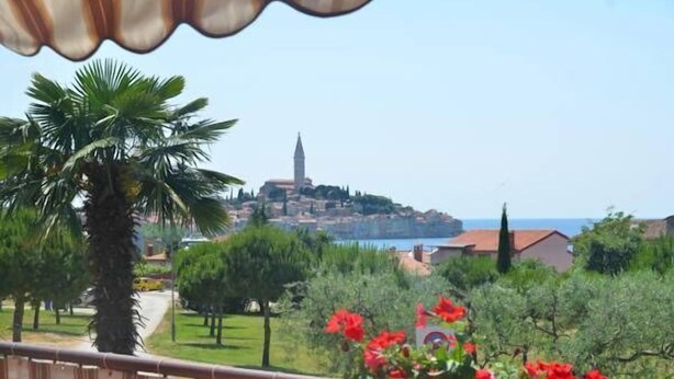 A coastal town with a prominent tower, lush greenery, and a clear view of the sea. - Apartments Palma (Rovinj)