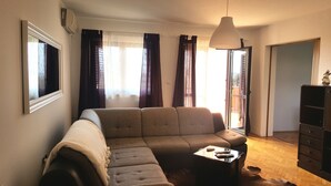 A living room with a sectional sofa, a coffee table, a hanging light fixture, a sliding glass door, and a wardrobe. - Apartments Palma (Rovinj)
