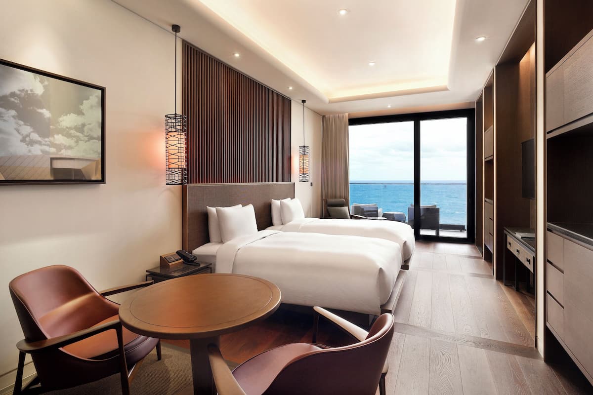 Ein modernes Hotelzimmer mit einem großen Bett, einem Schreibtisch, zwei Stühlen, einem Fernseher und Blick auf das Meer.