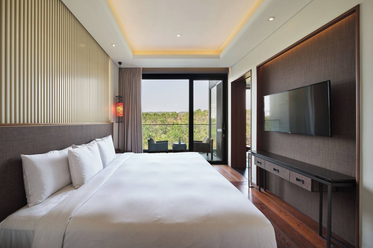 Ein modernes Hotelzimmer mit einem großen Bett, einem Flachbildfernseher und einem Balkon mit Blick auf die Stadt.
