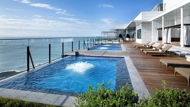Ein moderner Poolbereich im Freien mit klarem, blauem Wasser, einer Holzterrasse und Liegestühlen.