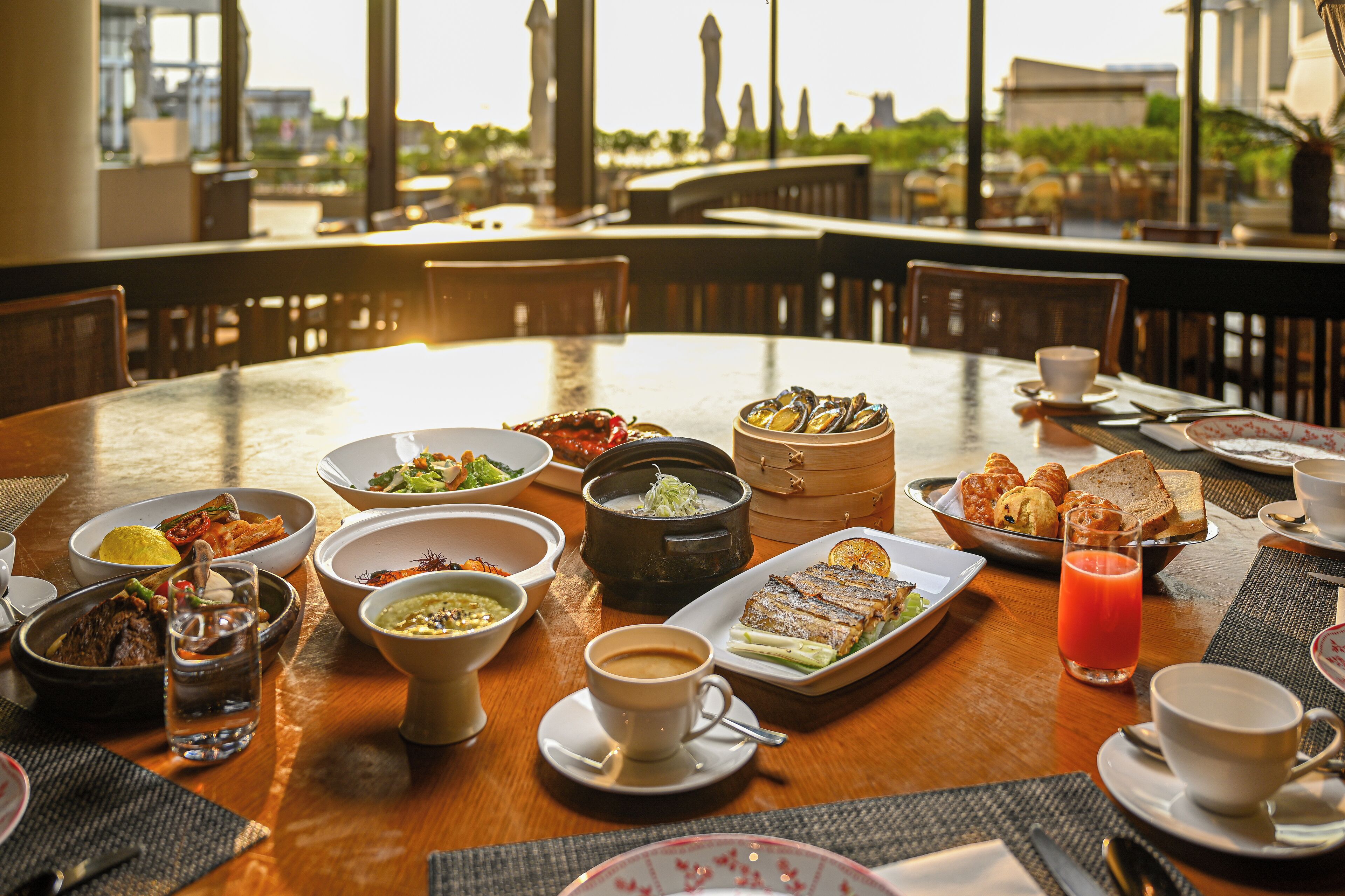 A dining table with various dishes, including seafood, bread, and a drink, set in a restaurant with a view of buildings and greenery.