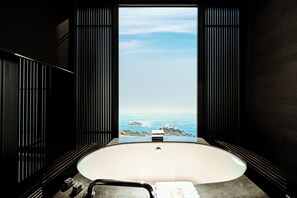 A modern bathroom with a large bathtub, a view of the ocean, and dark wooden paneling.