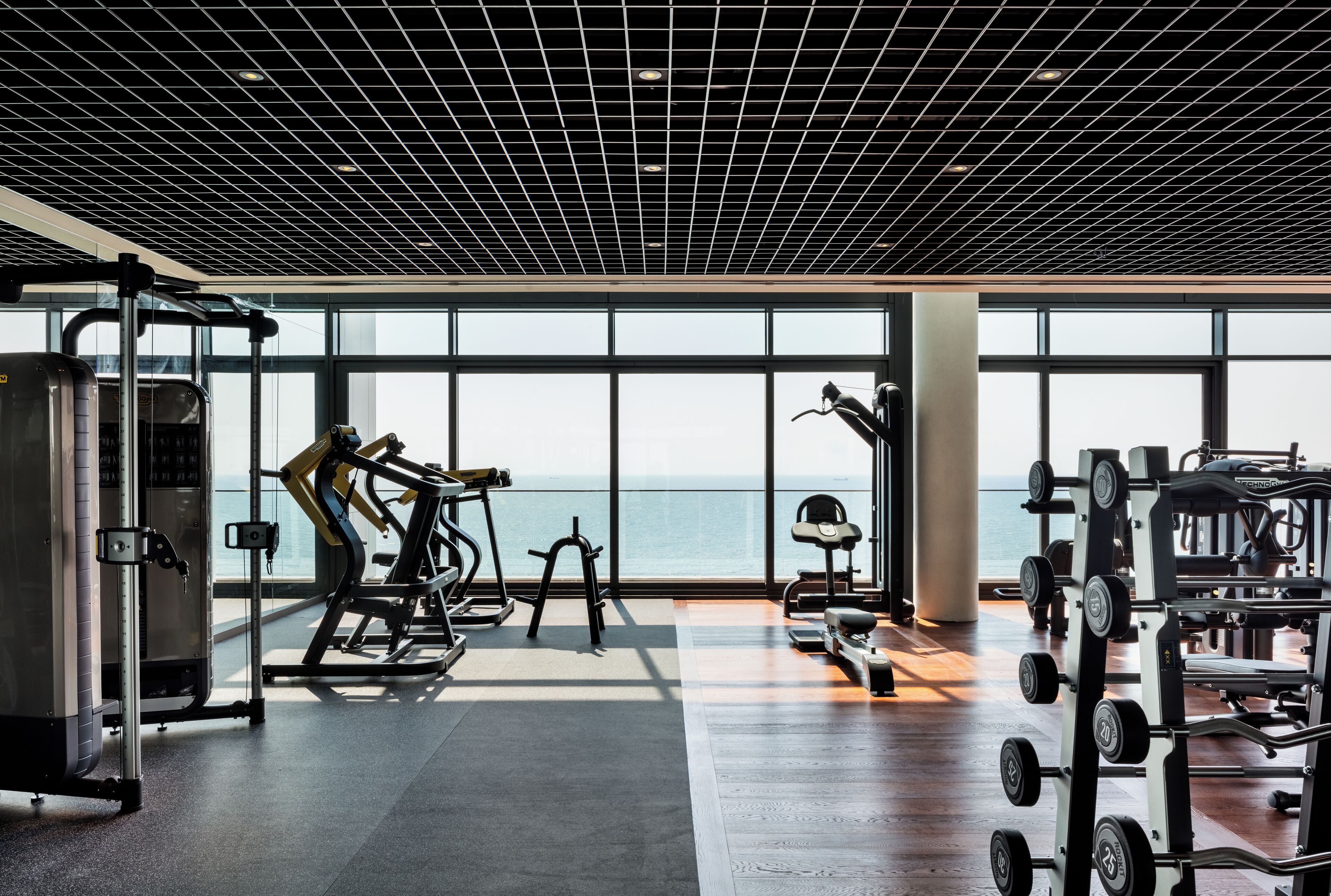 Une salle de sport dotée de grandes fenêtres, d’équipements d’exercice et offrant une vue sur la mer.
