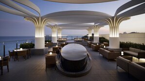 Eine moderne Lounge-Bereich im Freien mit Sitzgelegenheiten und einer zentralen Wasserspende, mit Blick auf ein Gewässer.
