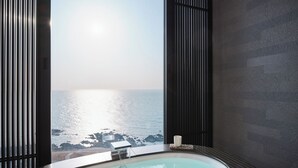 Ein modernes Badezimmer mit Eckjacuzzi, Meerblick und dunkel strukturierten Wänden.