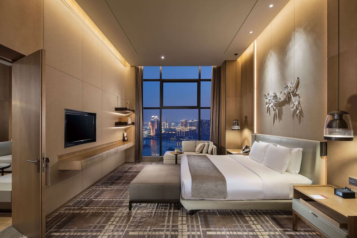 Une chambre d’hôtel moderne dotée d’un grand lit, d’une télévision, d’un bureau et offrant une vue sur le paysage urbain grâce à de grandes fenêtres.