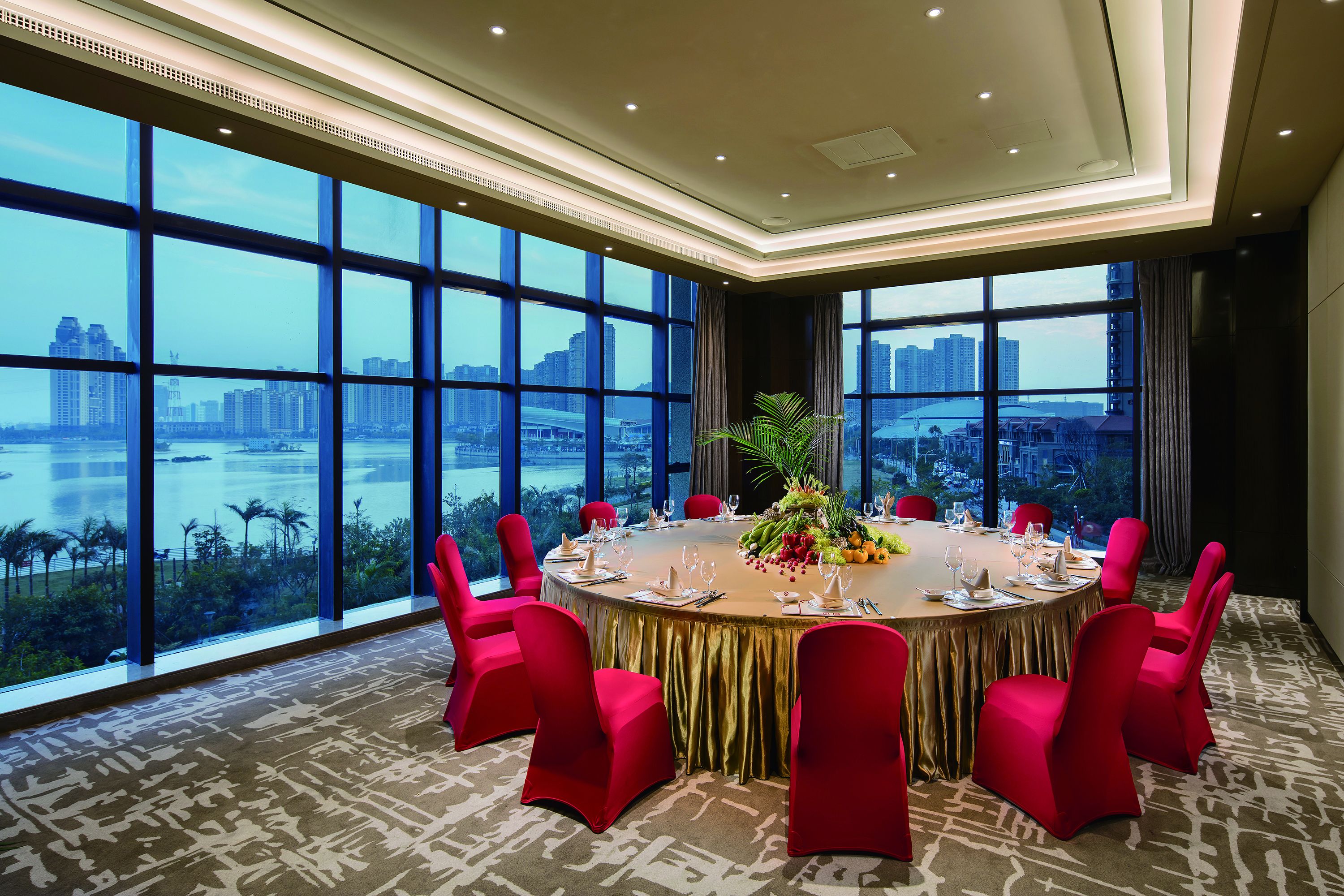 A conference room with a round table, red chairs, and a city view through large windows.