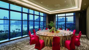 A conference room with a round table, red chairs, and a city view through large windows.
