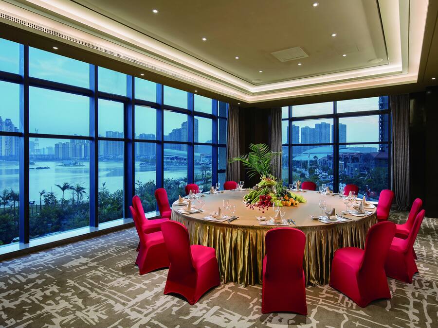 A conference room with a round table, red chairs, and a city view through large windows.