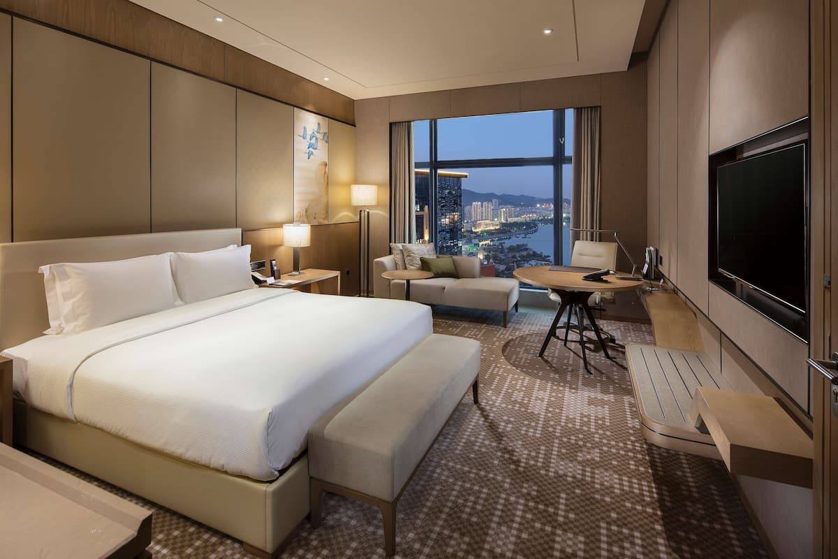 Une chambre d’hôtel avec un grand lit, un bureau, une chaise, une télévision et une vue sur la ville.