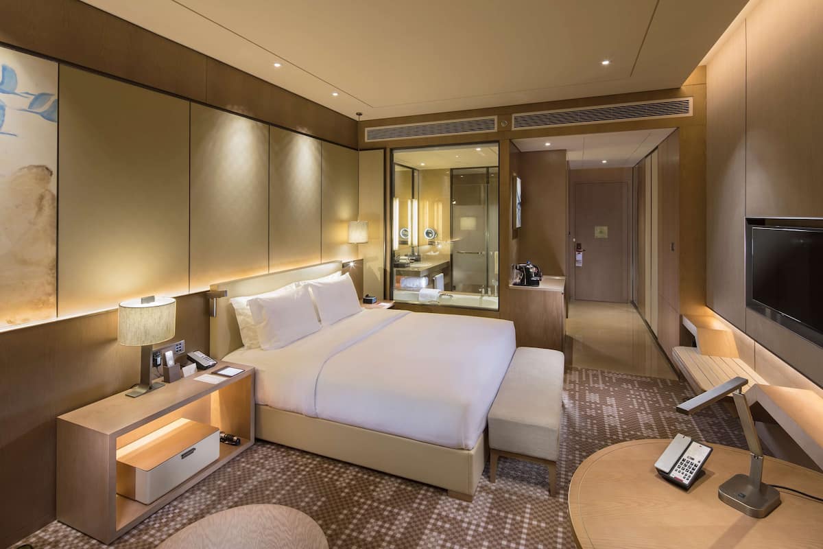 Une chambre d’hôtel moderne dotée d’un grand lit, de tables de chevet, d’une télévision et d’une salle de bain avec un miroir et un lavabo.