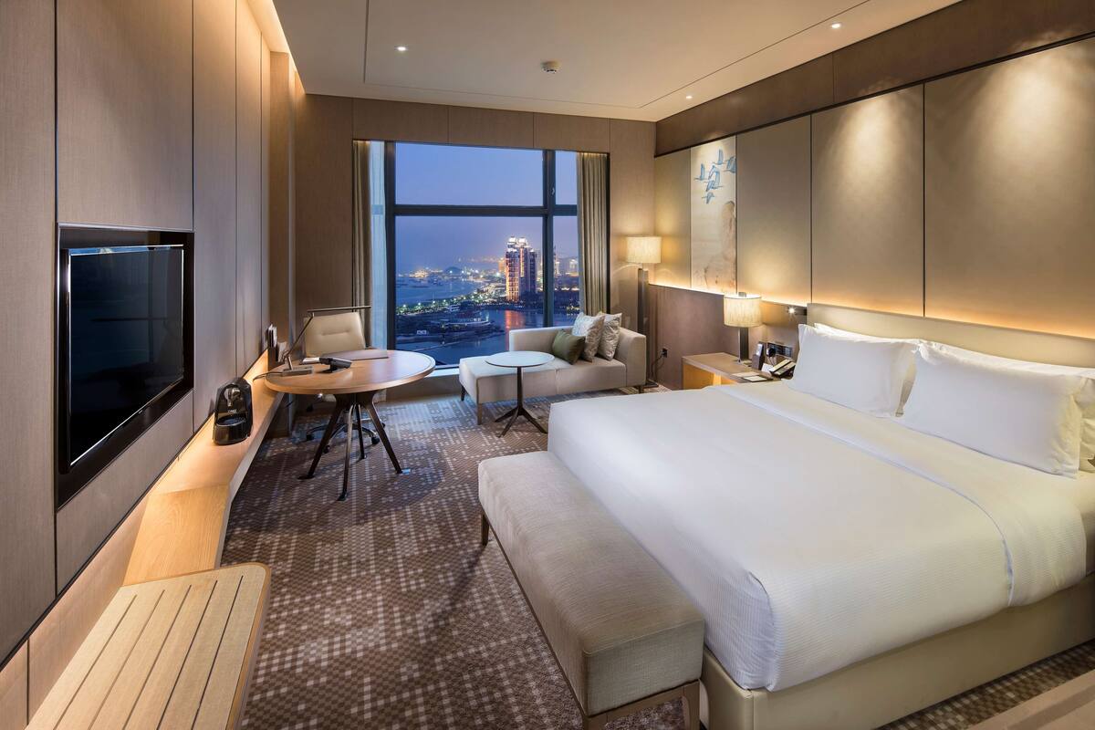Une chambre d’hôtel moderne dotée d’un grand lit, d’un coin salon avec une table, d’une télévision et offrant une vue sur le paysage urbain.