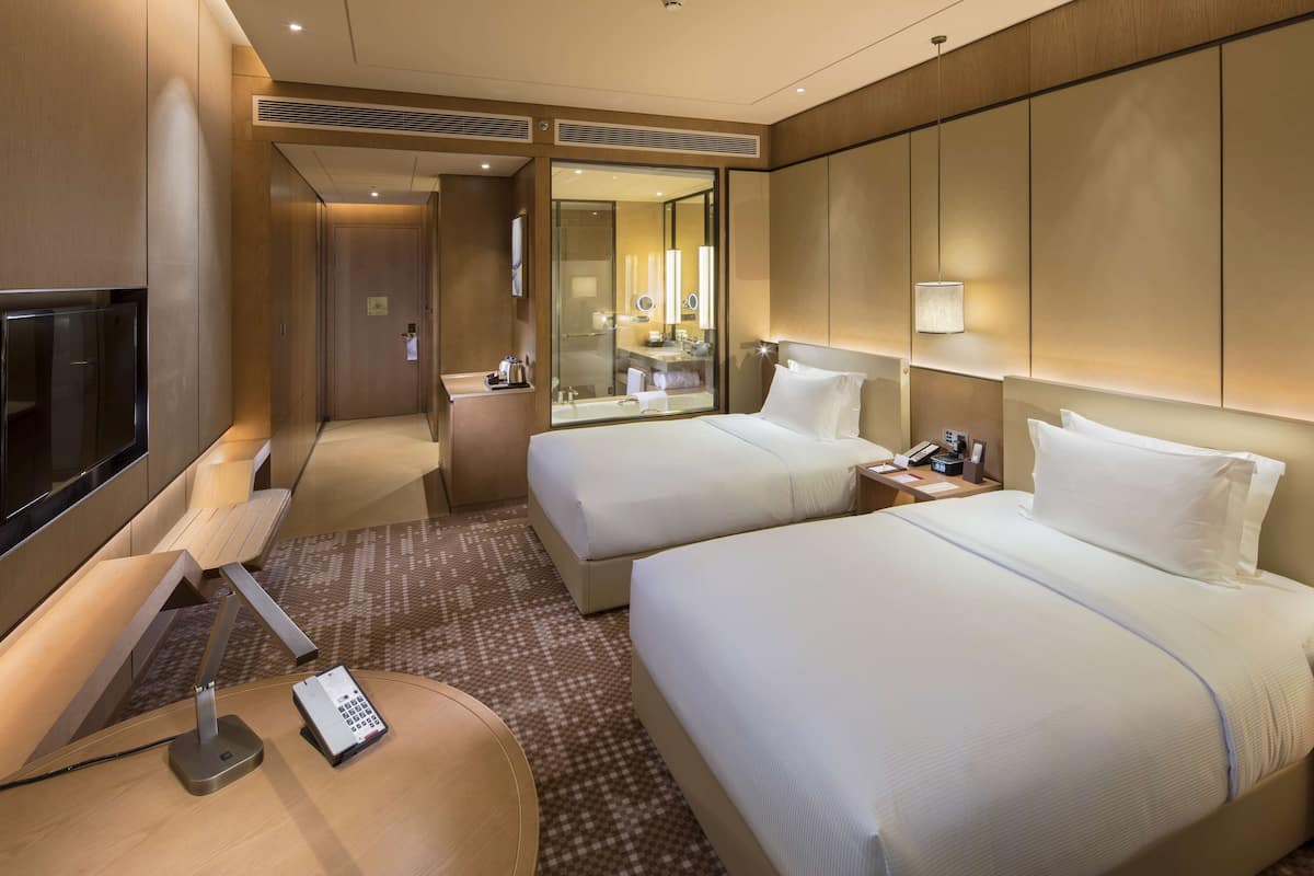 Une chambre d’hôtel avec deux lits, un bureau avec une lampe, une télévision et un minibar.