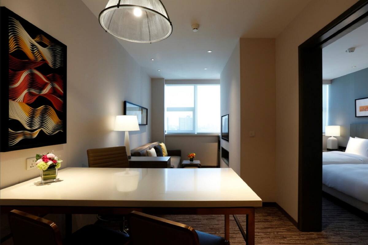 A hotel room with a dining table, a sofa, a bed, and a large window.
