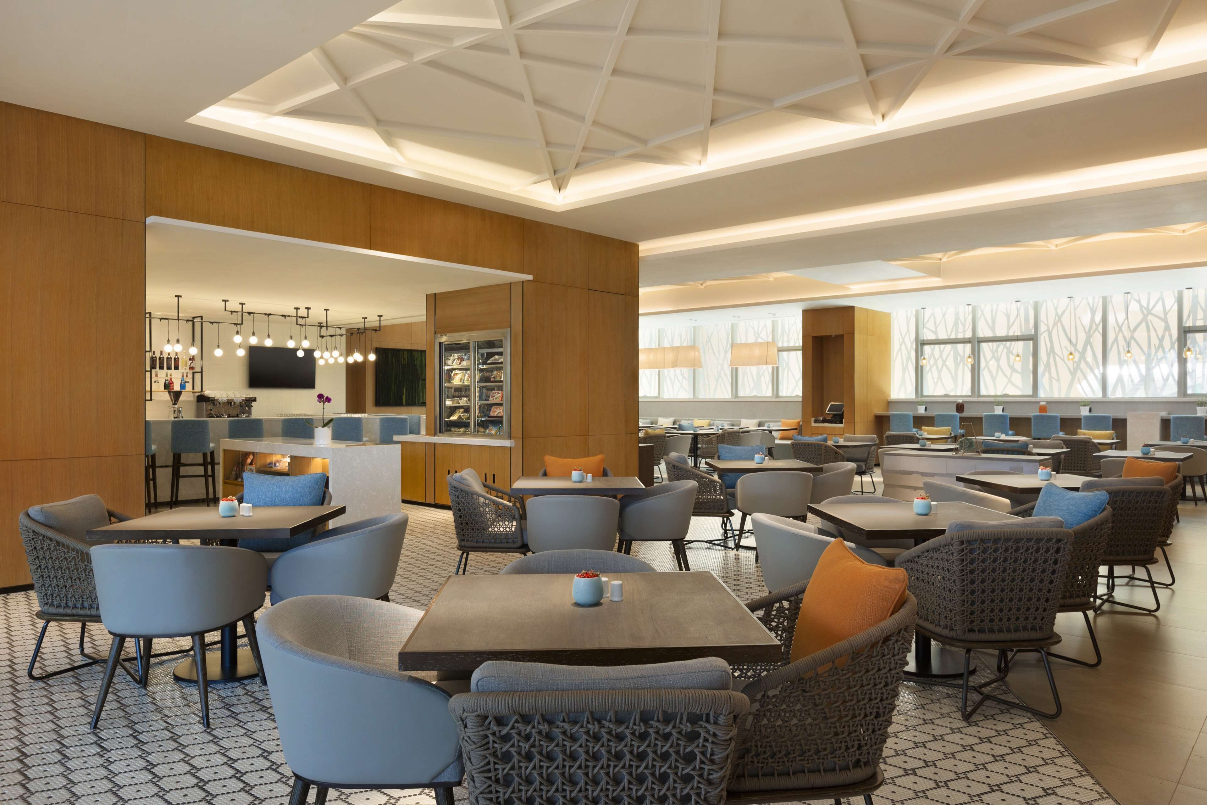 Un restaurant moderne doté de plusieurs espaces de restauration, d’un bar et d’une cuisine visible au fond de la salle.