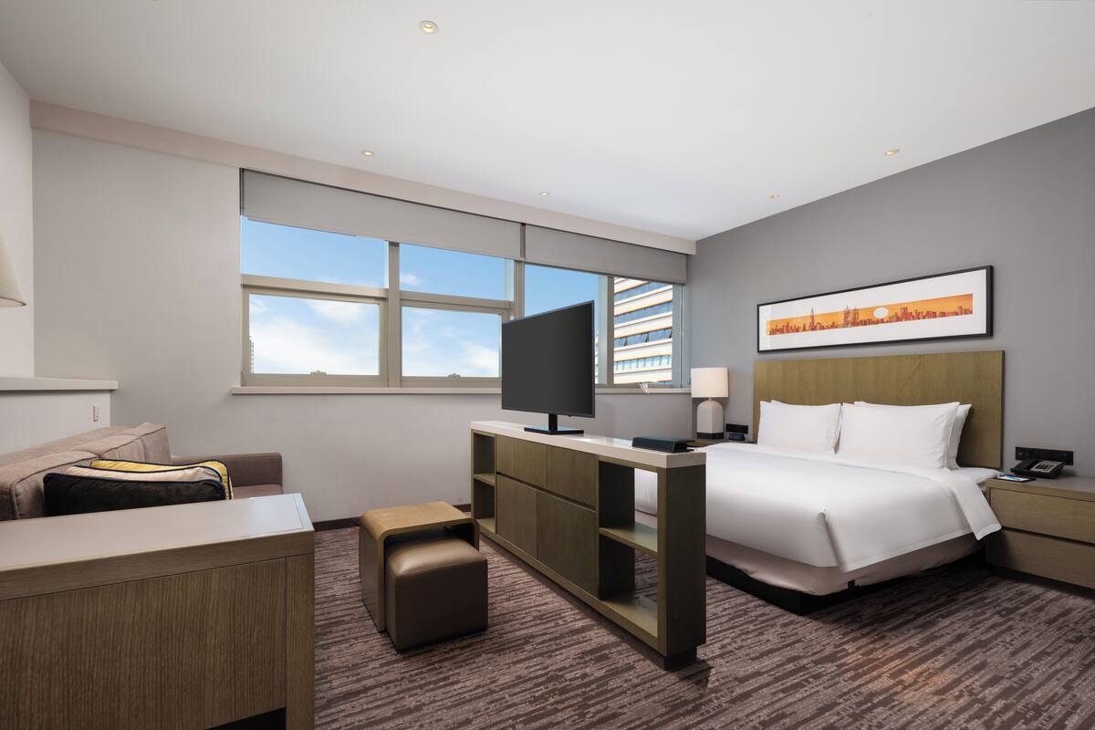 A hotel room with a bed, desk, television, and a large window.