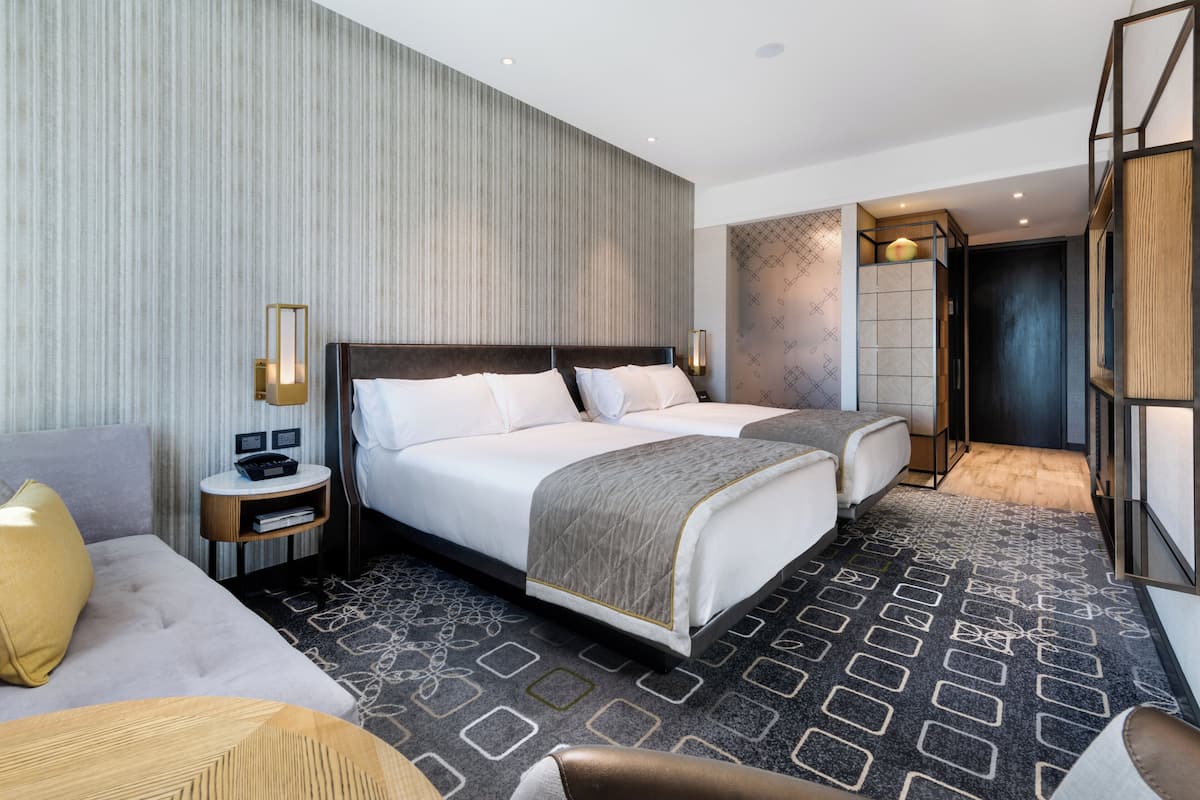 A modern hotel room with a large bed, two bedside tables, a sofa, and a decorative wall panel.