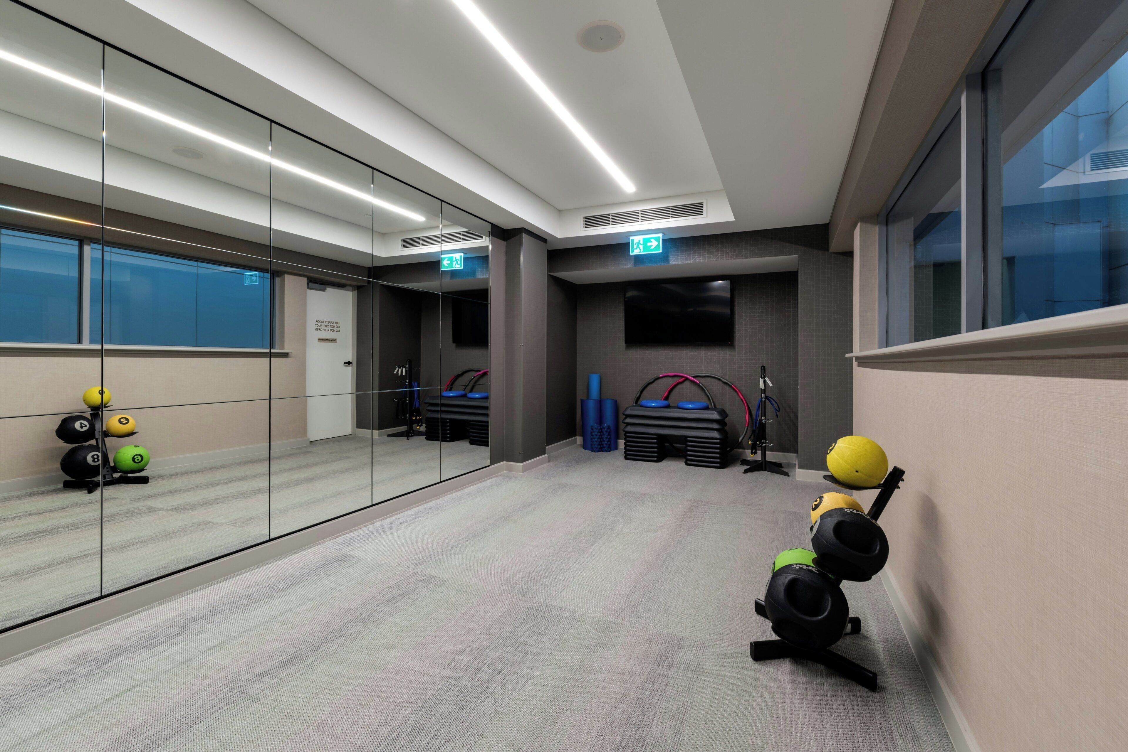 Un gimnasio con equipo de ejercicio, un espejo y una puerta con la indicación 'Exit'.
