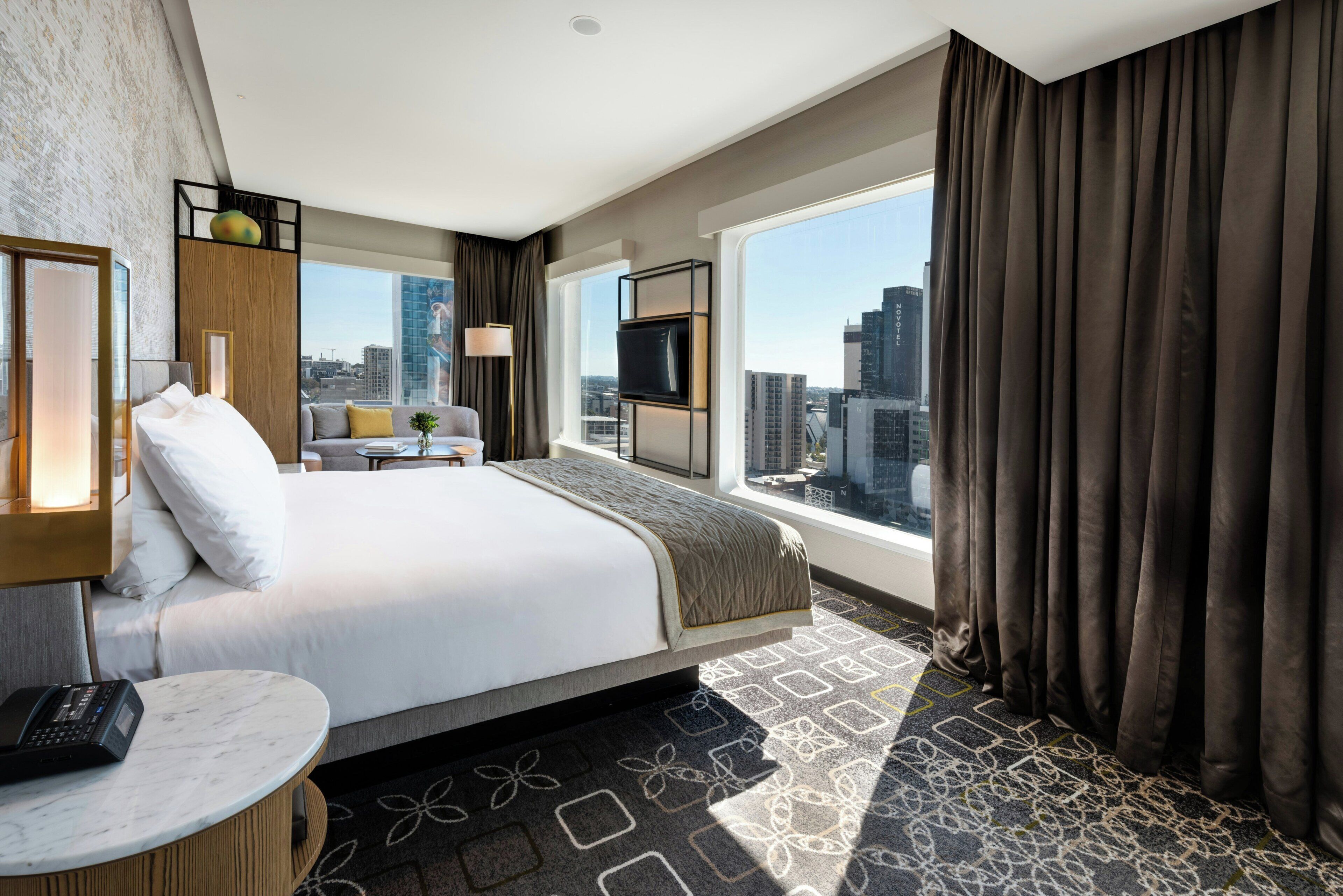Hotelkamer met een bed, een bureau, een stoel, een raam met gordijnen en uitzicht op de stad.