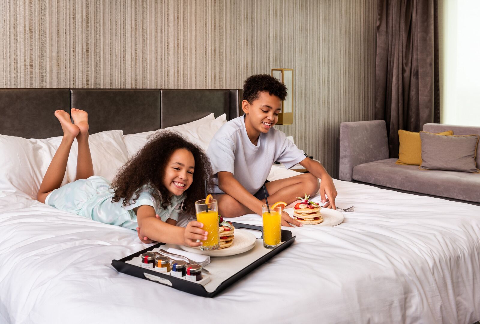 Een hotelkamer met een bed, een dienblad met ontbijtartikelen en een bank op de achtergrond.