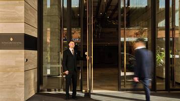 A man in a suit standing at the entrance of a building with a sign that reads 'Intercontinental Perth City Centre.'