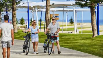 A pathway with people walking and cycling, surrounded by greenery and a clear sky.