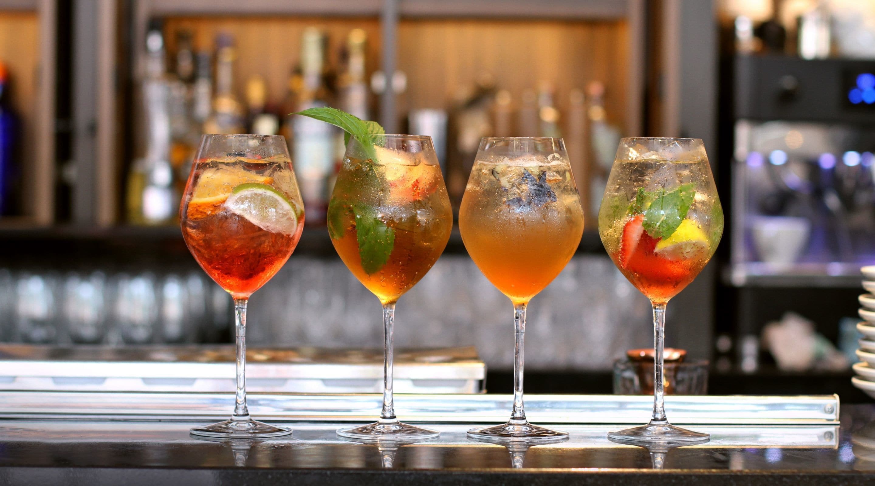 Tres copes de còctel amb gel i guarniments damunt un taulell de bar.