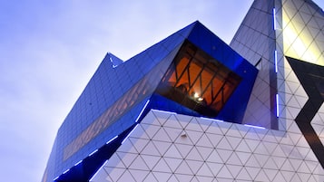 A modern architectural building with a unique geometric design, featuring a prominent angular structure and a large glass facade.
