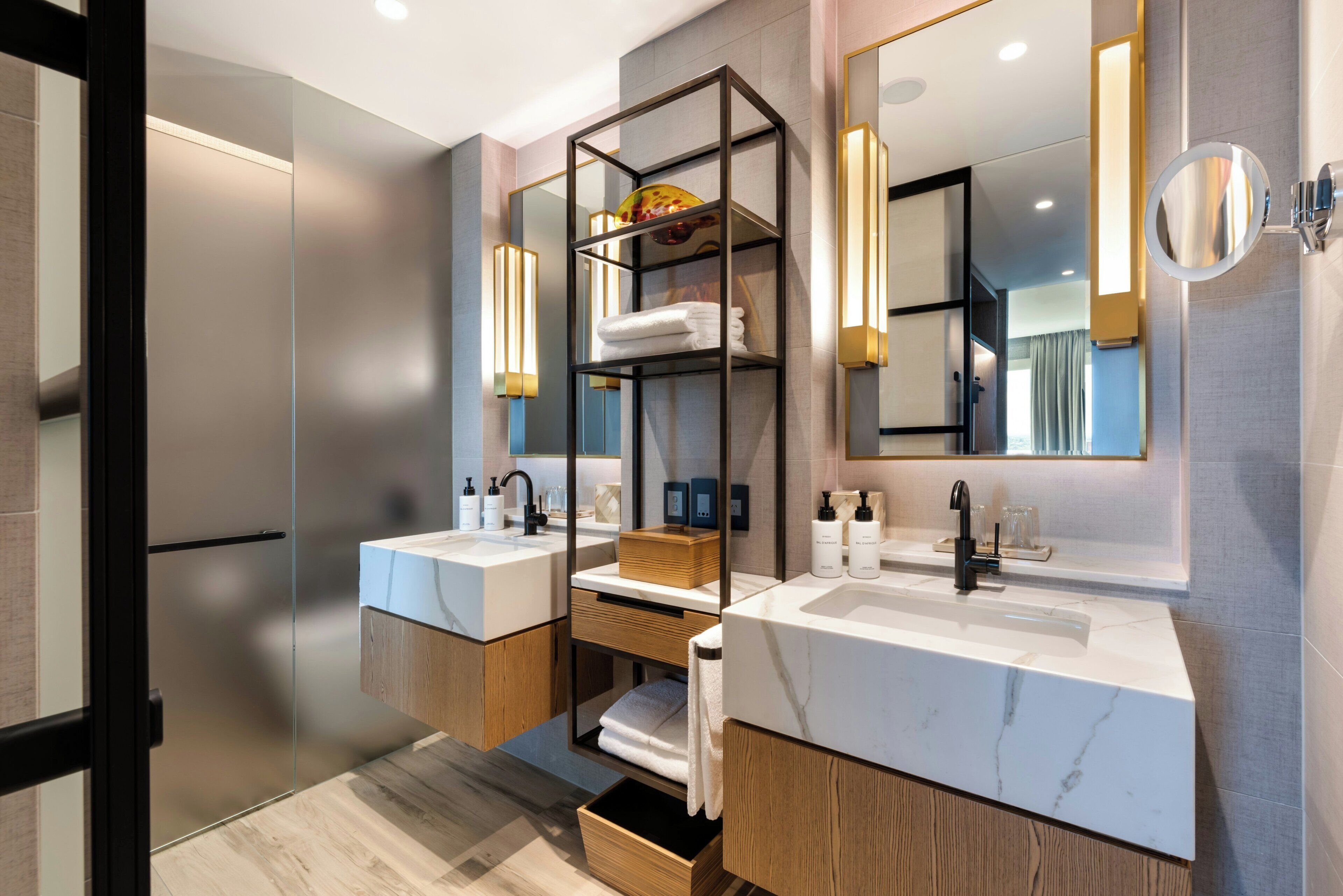 Un baño moderno con dos lavamanos, armarios de madera y un estante empotrado con toallas.
