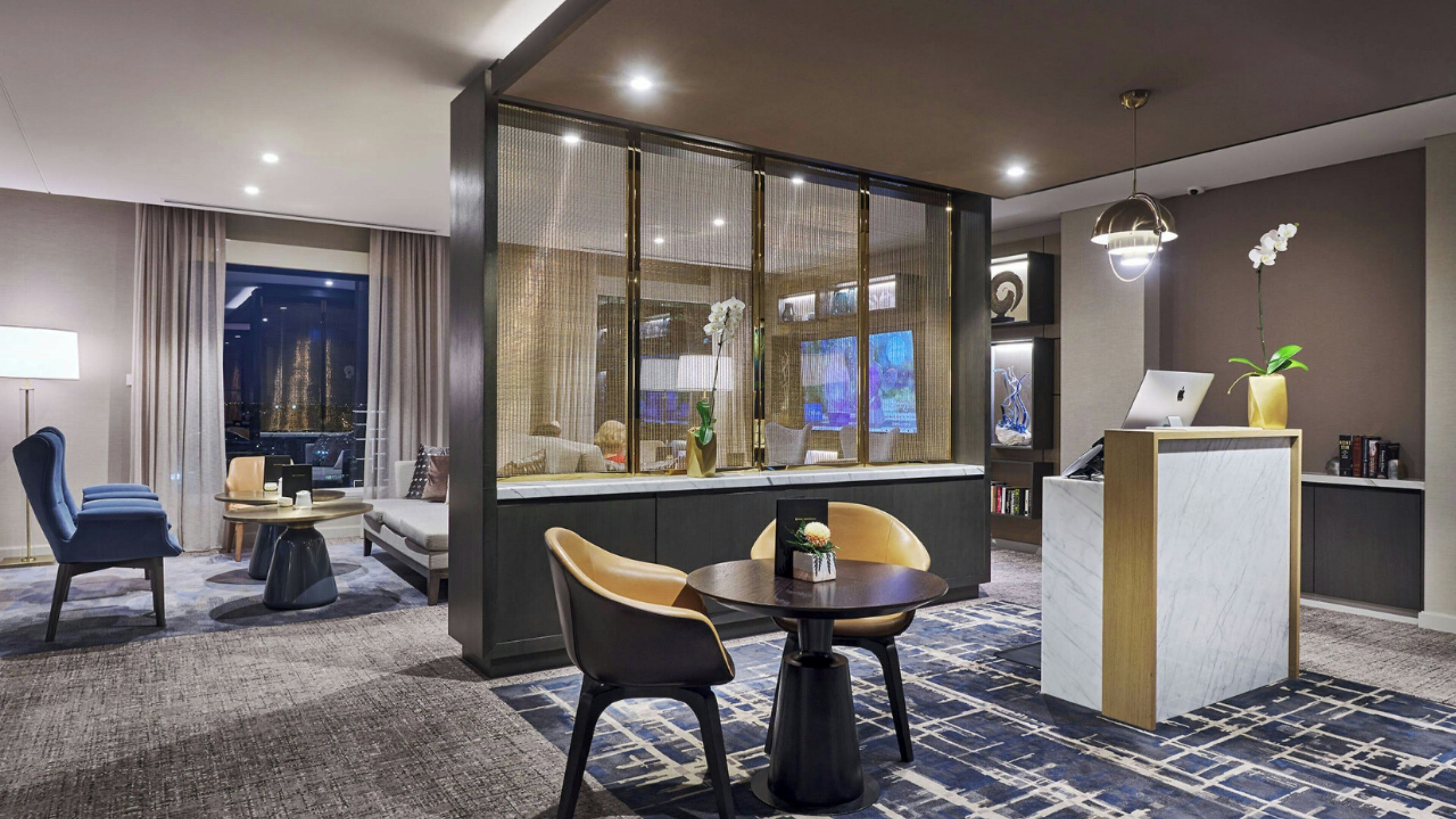 A modern hotel room with a seating area, a desk, and a large window with curtains.