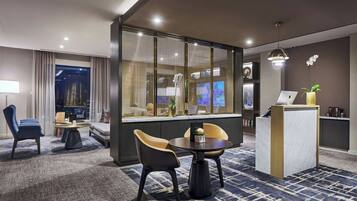 A modern hotel room with a seating area, a desk, and a large window with curtains.